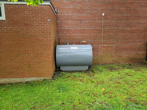 An aboveground oil tank sits next to a brick wall.